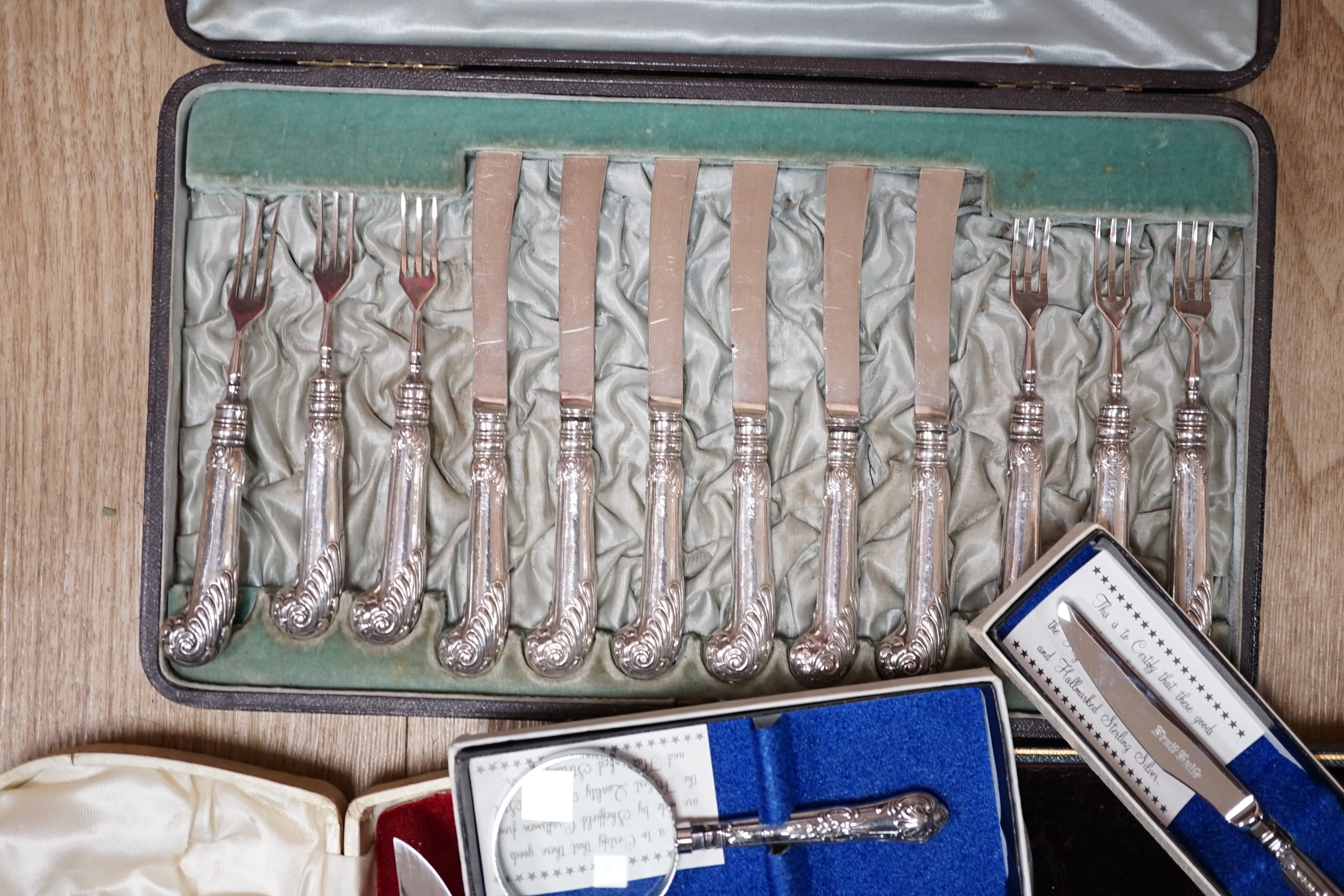 Two cased plated carving sets, a cased set of silver handled cake knives, a modern silver handled magnifying glass and cake slice.